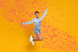 Happy woman jumping under flying confetti on orange background