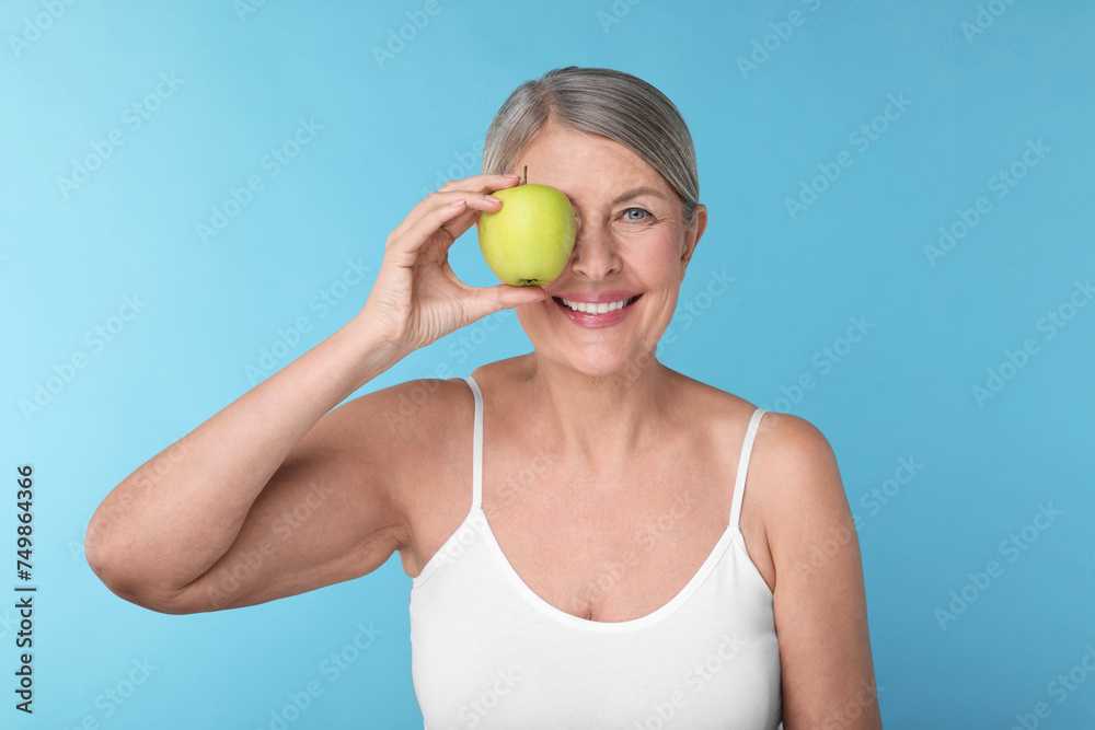 Beautiful woman with fresh apple on light blue background. Vitamin rich food Beautiful woman with fresh apple on light blue background. Vitamin rich food