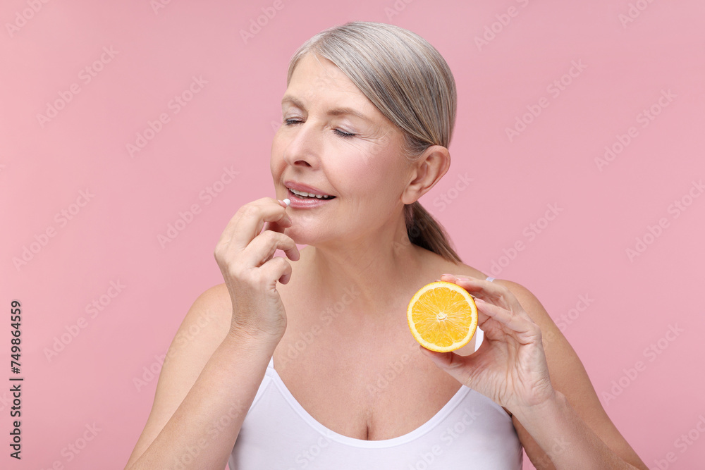 Beautiful woman with half of orange taking vitamin capsule on pink background Beautiful woman with half of orange taking vitamin capsule on pink background