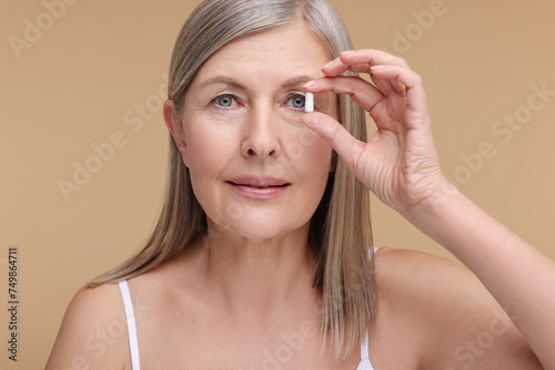 Beautiful woman with vitamin capsule on beige background
