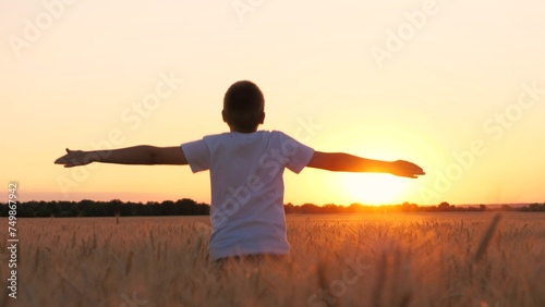 Happy male teen running on wheat field with open hands enjoy freedom at sunset sunrise back view closeup. Boy kid teenager relaxing imagine flying at dusk rye meadow sun sky forest horizon