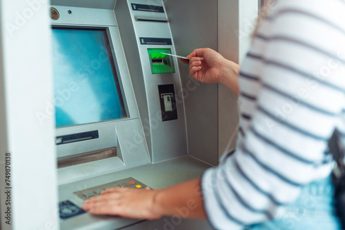 Awoman puts a credit card into an ATM to withdraw money.