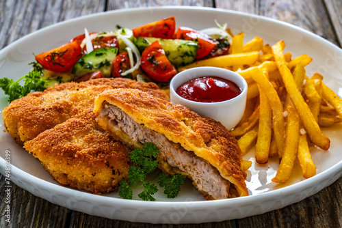 Crispy breaded fried pork loin chops with fries and fresh vegetables on wooden table
