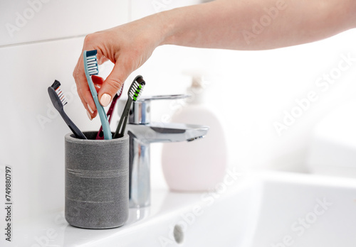 Woman'S Hand Picks One Of 4 Toothbrushes In Bright Bathroom