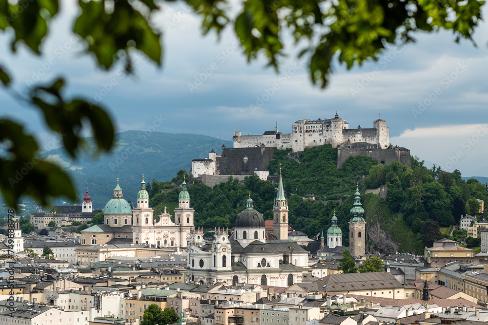 Fototapeta premium An early summer cloudy day in the historic centre of Salzburg in Austria framed with green leaves of a tree