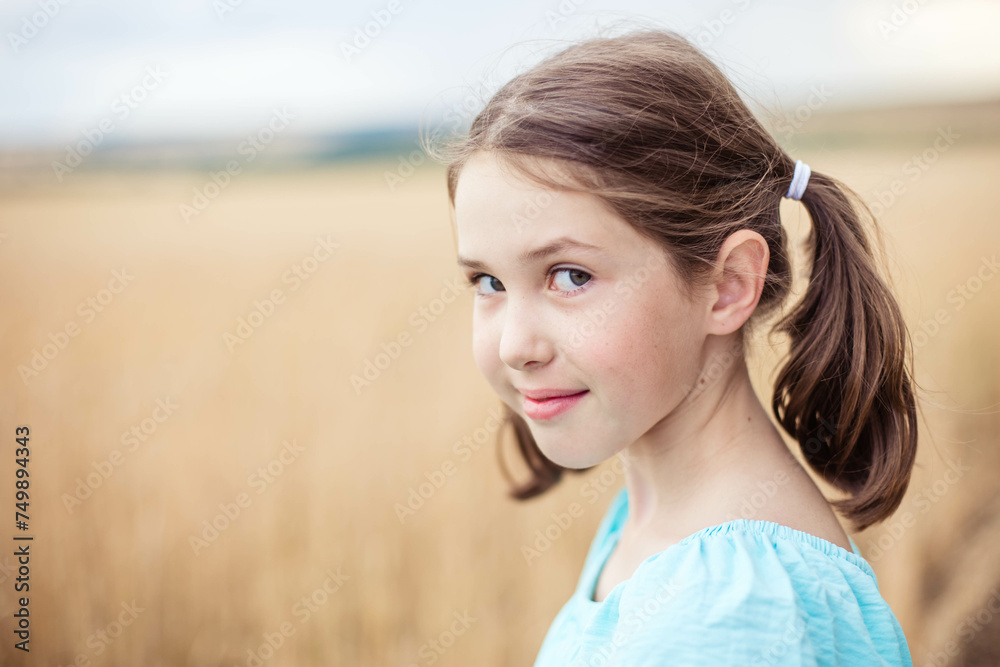 Close-up portrait of a cute teenage girl looking at the camera on the background of a summer field.