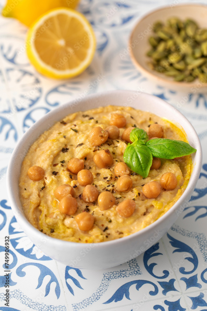 A bowl of hummus with chickpeas and basil on a table A bowl of hummus with chickpeas and basil on a table