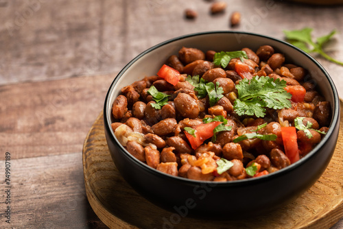 Food dish made of beans, tomatoes, and cilantro on a wooden table