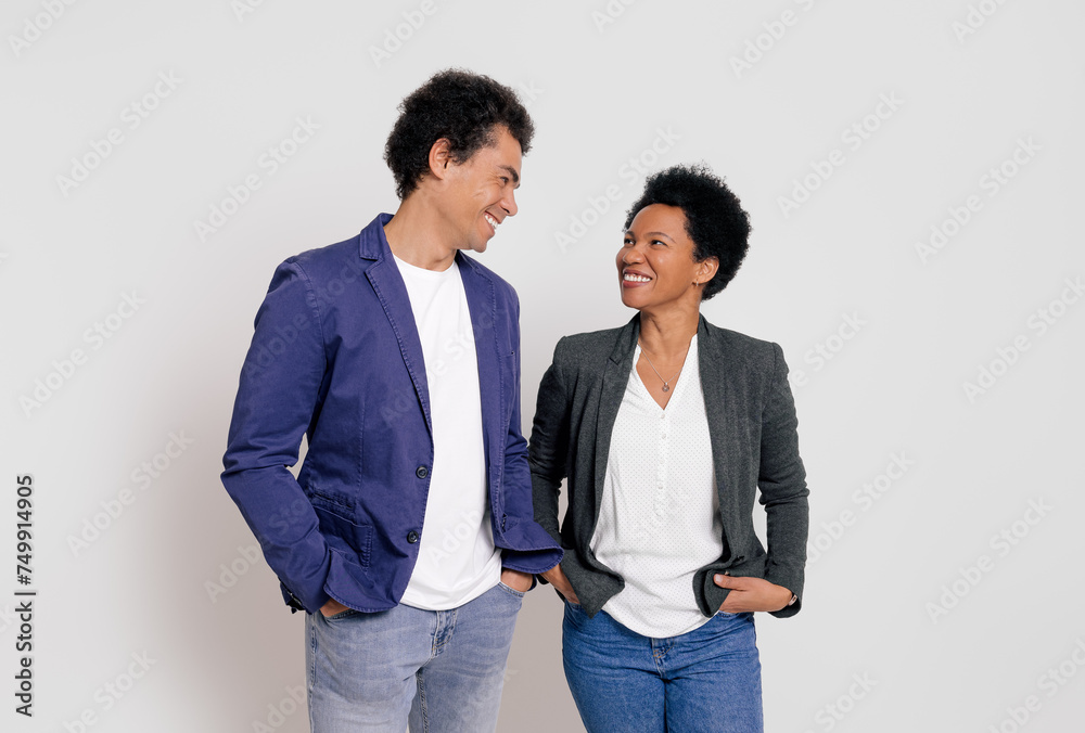 Happy young coworkers with hands in pockets looking at each other while standing on white background Happy young coworkers with hands in pockets looking at each other while standing on white background