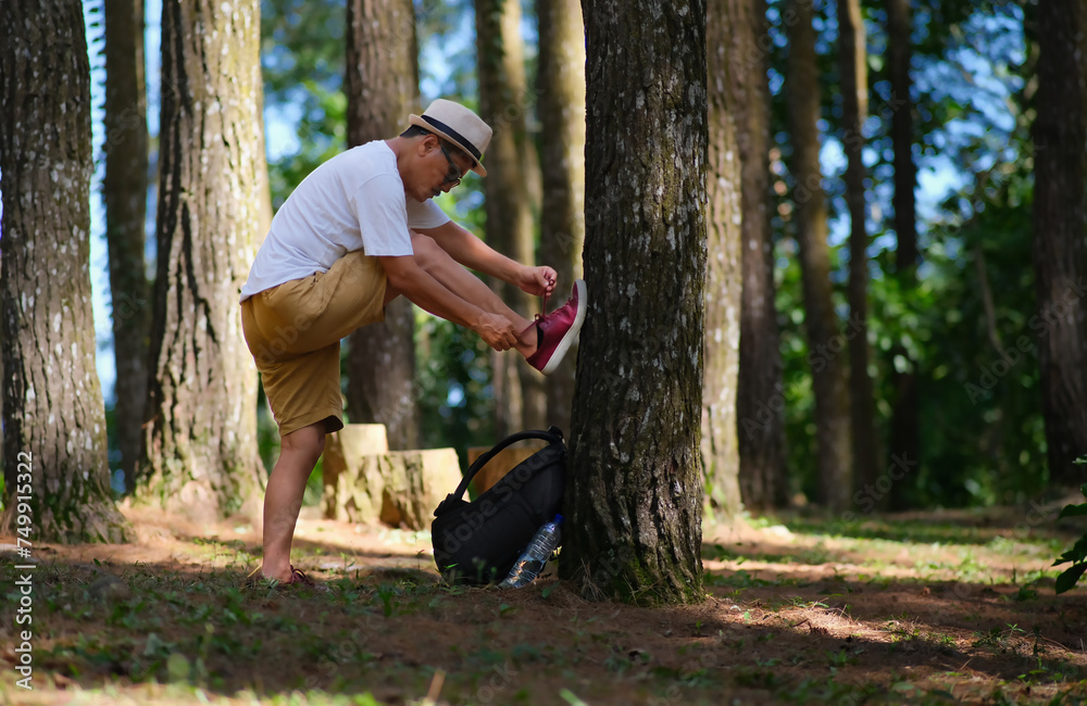 A guy fixing his shoe lace on a tree while hiking across pine woods