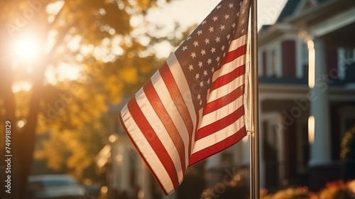 An American flag waves gently in focused foreground of a peaceful suburban neighborhood at sunset