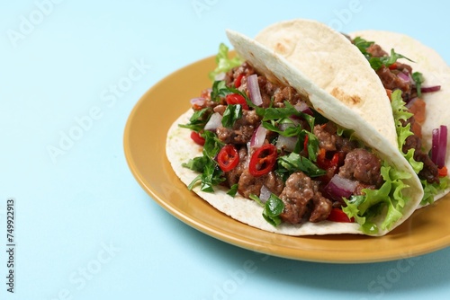Delicious tacos with meat and vegetables on light blue table, closeup