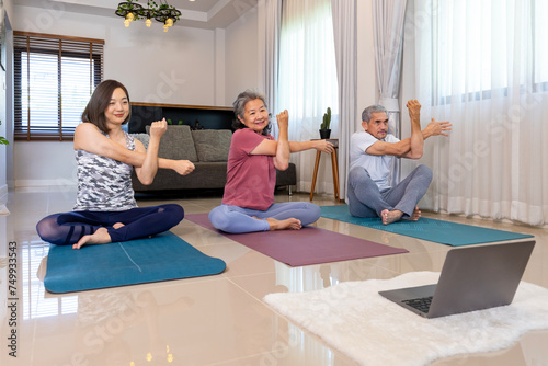 Senior asian couple and daughter are exercising at home doing sitting meditation yoga pose with online trainer class from internet for elder healthy and longevity concept