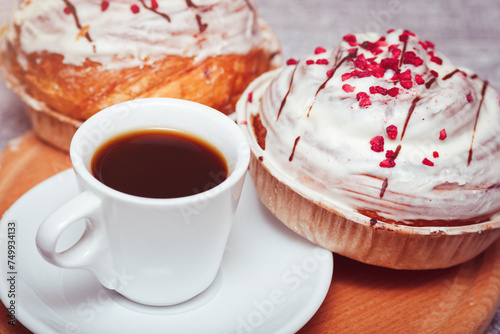 The cup of espresso coffee with cinnabon sweet buns. Tasty pastry with cream glaze and pink decoration.
