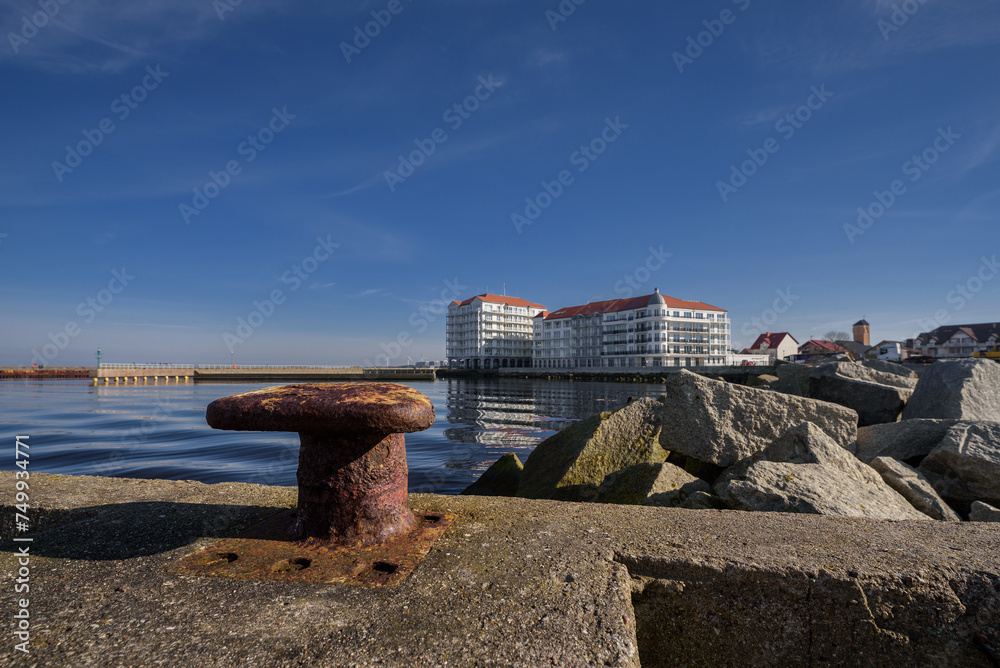 Obraz premium A CITY BY THE SEA - Old rusty bollard on the port quay and a holiday resort in the background