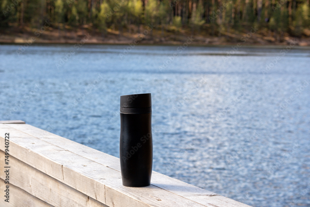 
Black thermos on wooden board with blue water background