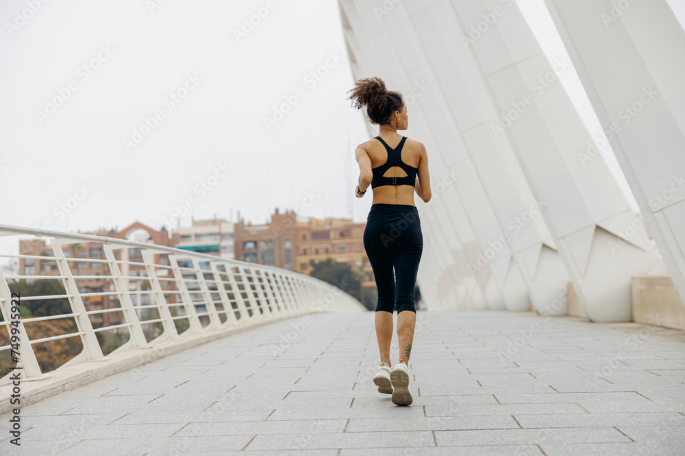 Back view of woman athlete is jogging on morning on modern building background. Healthy life concept Back view of woman athlete is jogging on morning on modern building background. Healthy life concept