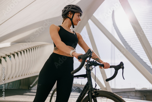 Woman cyclist in protective gear standing with her bike while training outdoors and looks away