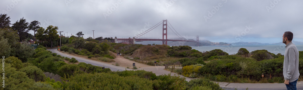Fototapeta premium A man enjoying the view of the Golden Gate Bridge from the Battery East Vista overlook at Presidio of San Francisco in San Francisco, California, USA.