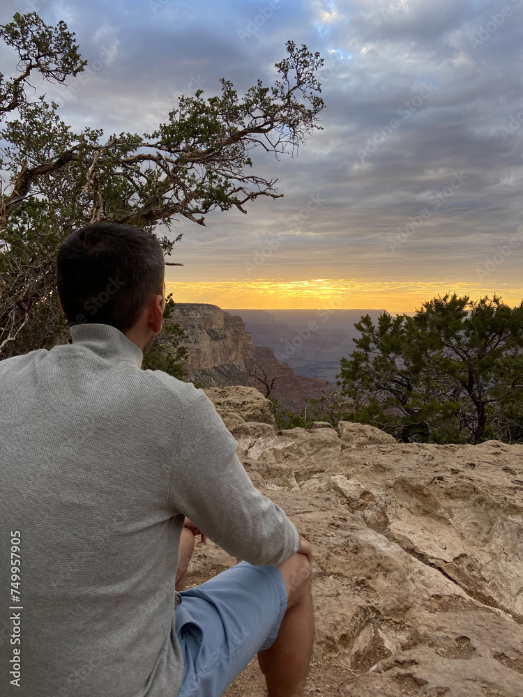 A tourist man enjoying the view of the South Rim of the Grand Canyon National Park at sunset.
