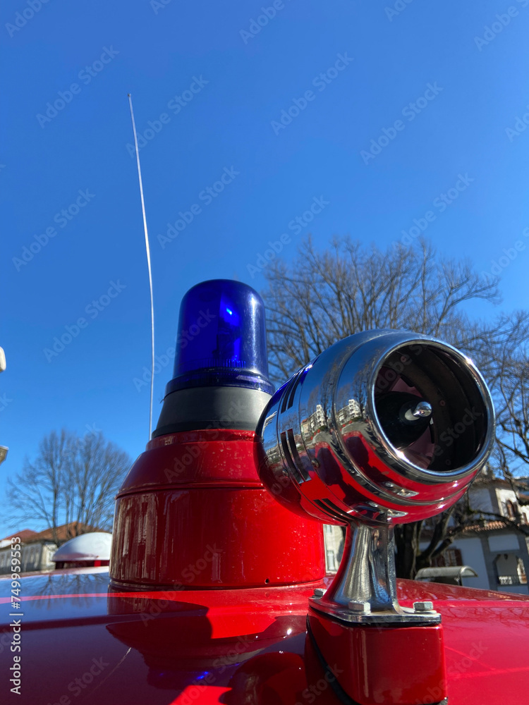 Vintage siren, antenna, and a blue rotating beacon on the roof of a red ambulance from the Santo Tirso Volunteer Firefighters on exhibition at Sao Bento Count Square in Portugal.