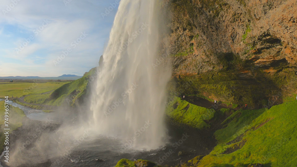 The Seljalandsfoss waterfall on the south coast of Iceland bathed in the otherworldly light of the midnight sun. The waterfall drops 60 meters and is part of the Seljalands River.
