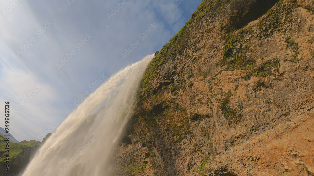 The Seljalandsfoss waterfall on the south coast of Iceland bathed in the otherworldly light of the midnight sun. The waterfall drops 60 meters and is part of the Seljalands River.