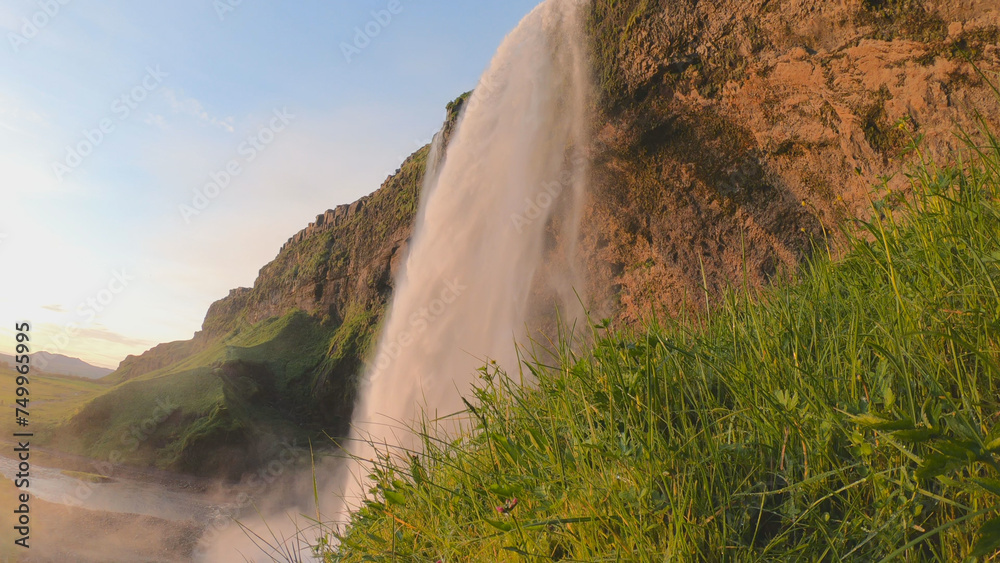 The Seljalandsfoss waterfall on the south coast of Iceland bathed in the otherworldly light of the midnight sun. The waterfall drops 60 meters and is part of the Seljalands River.