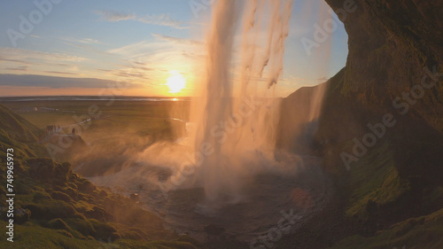 The Seljalandsfoss waterfall on the south coast of Iceland bathed in the otherworldly light of the midnight sun. The waterfall drops 60 meters and is part of the Seljalands River. photo