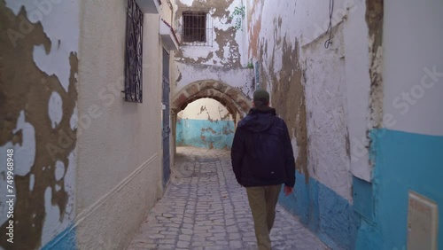 A man walks along a narrow street in the Old Medina. Shooting from the back.