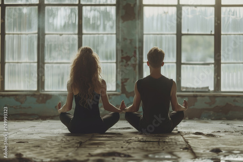 Yoga group concept. Young couple meditating together  sitting back to back on windows background.