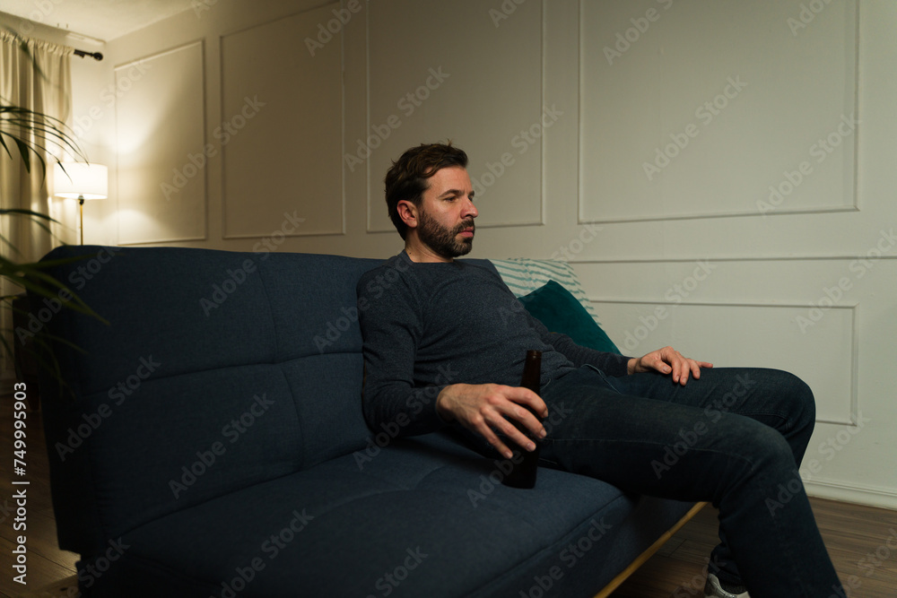Lonely man sitting on the couch alone drinking beer looking sad Lonely man sitting on the couch alone drinking beer looking sad