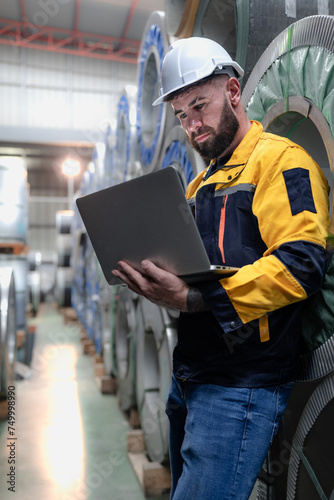 Industrial engineer in safety helmet uniform jacket working in heavy steel engineering factory. Technician manager worker inspector using laptop in metalwork product manufacturing facility workplace