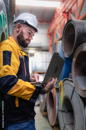 Industrial engineer in safety helmet uniform jacket working in heavy steel engineering factory. Technician manager worker inspector using laptop in metalwork product manufacturing facility workplace