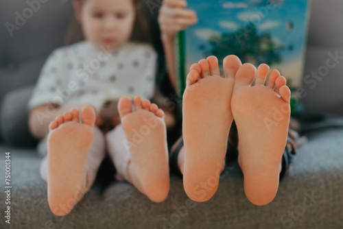 Big brother and little sister holding bare feet close up to camera . Blurred face on background 