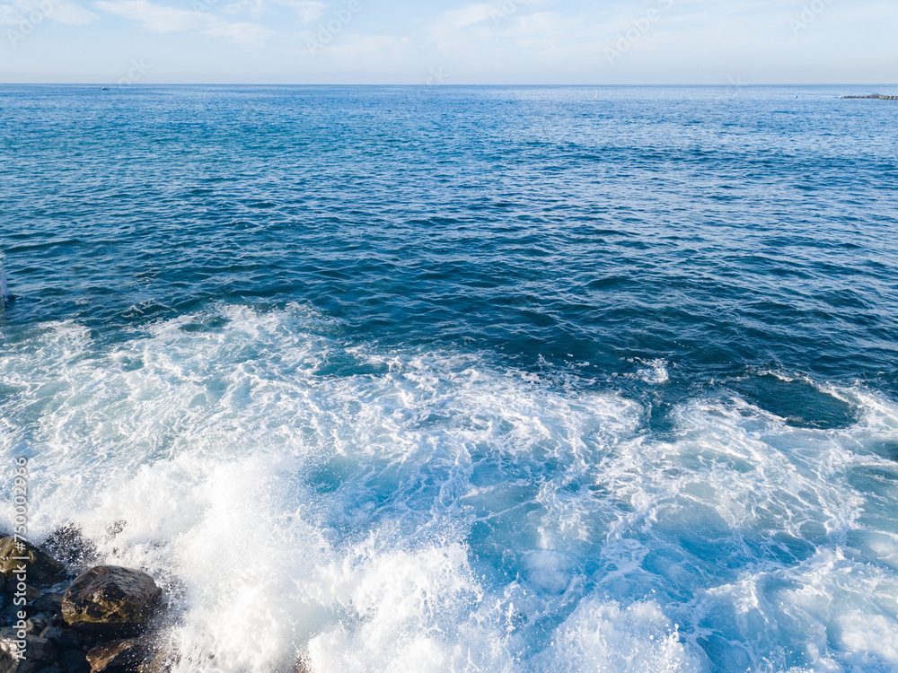 Fototapeta premium Rocky beach with Atlantic Ocean waves meeting with underwater sharp rocks. Blue sea with small waves with foam crashing on the beach, south of Tenerife, Canary Islands
