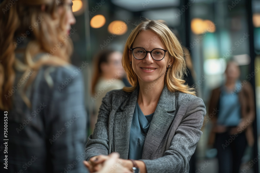 middle-aged businesswoman with specs shaking hands with other women in an office space background.
