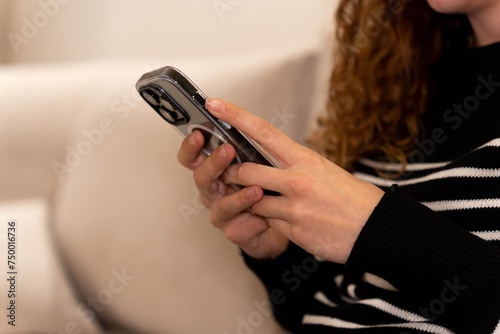 A woman is sitting on a couch and looking at her cell phone. She is holding the phone in her hand and she is focused on the screen
