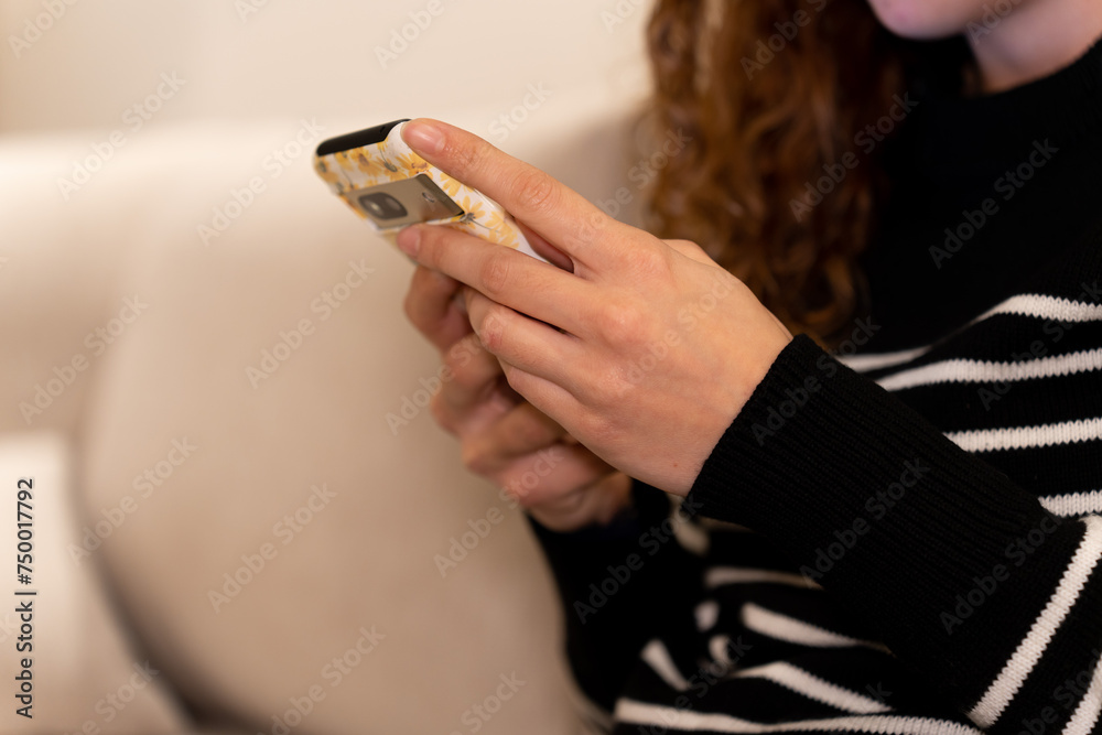 A woman is sitting on a couch and looking at her cell phone. She is holding the phone in her hand and she is focused on the screen