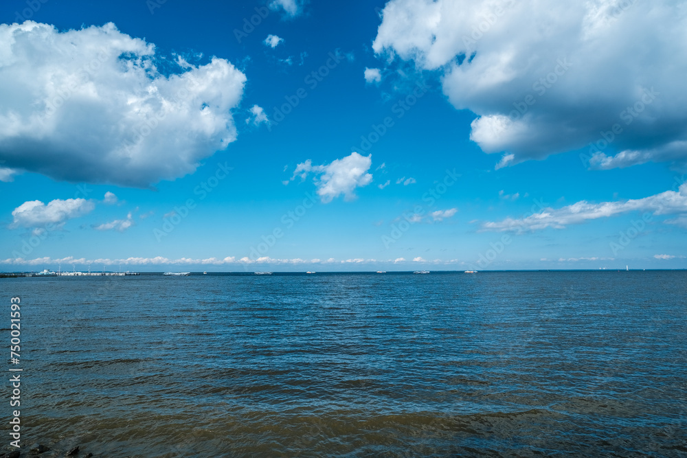 View from the shore to the sea bay in summer. The sky above the water with white clouds.