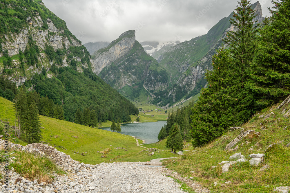 Hikinig trail towards Seealpsee, an alpine lake in Appenzell Alps in Switzerland. Easey walking path to an alpine lake, pine trees on the side of the trail, alpine lake between steep mountains. Swiss.