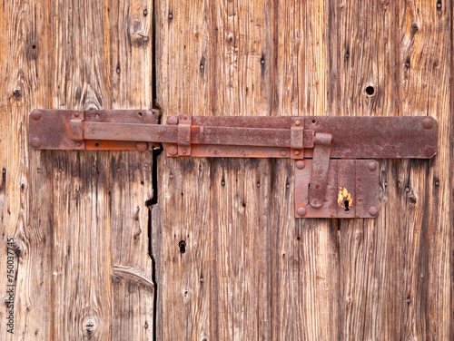 An old wooden door with a hinged vintage iron bolt. Rusty massive iron lock on an abandoned wooden gate. Sun-faded, aged and bark beetle-eaten wooden doors. Rovinj, Croatia - February 29, 2024