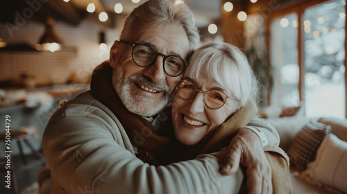 Portrait of couple of happy mature people in love hugging and looking at the camera smiling and having fun at home. Two cute seniors enjoying indoors together.