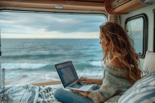 A woman sitting in an RV working on laptop. The background is the ocean