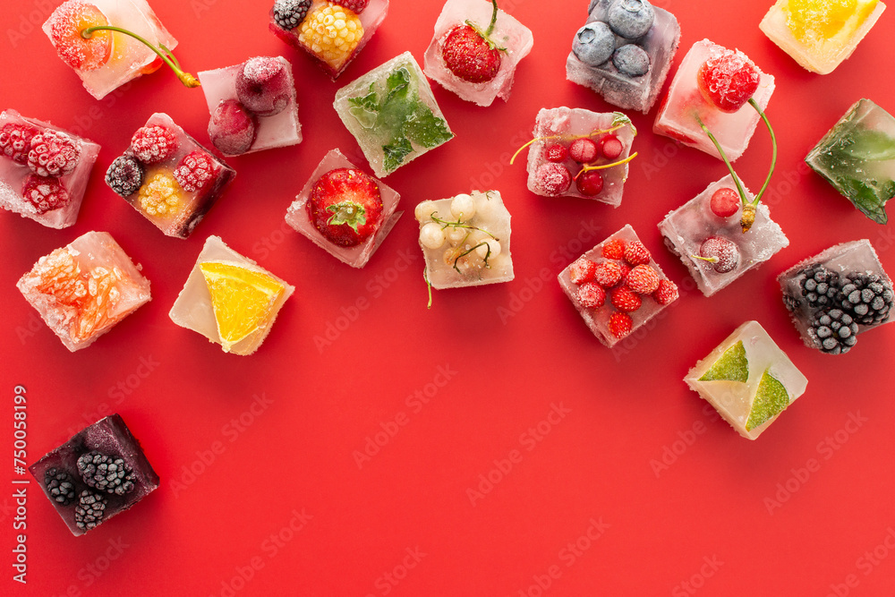 Red background with ice cubes with frozen berries and fruits and mint