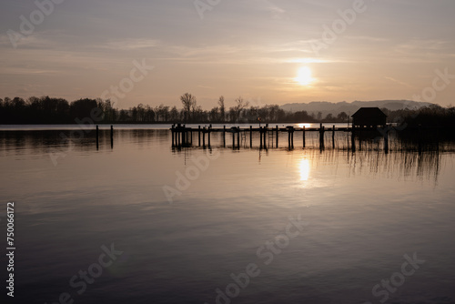 As the sun begins its descent, the lake takes on a golden glow, the reflection of the fading day painting the waters with warm hues. 