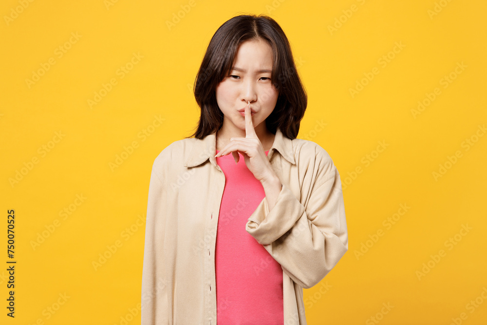 Young woman of Asian ethnicity wears pink t-shirt beige shirt pastel casual clothes say hush be quiet with finger on lips shhh gesture isolated on plain yellow background studio. Lifestyle portrait. Young woman of Asian ethnicity wears pink t-shirt beige shirt pastel casual clothes say hush be quiet with finger on lips shhh gesture isolated on plain yellow background studio. Lifestyle portrait.