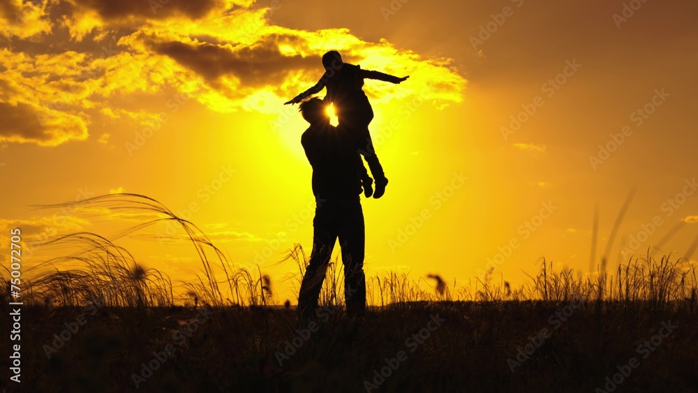 Dad plays with his child son, throws child up into sky with his hands, happy child smiles. Father child son, play together in park in front of sun, Silhouette. Family happiness concept . Child is fly