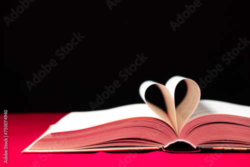 The pages of the book are folded in the shape of a heart on a pink and black background, place for text