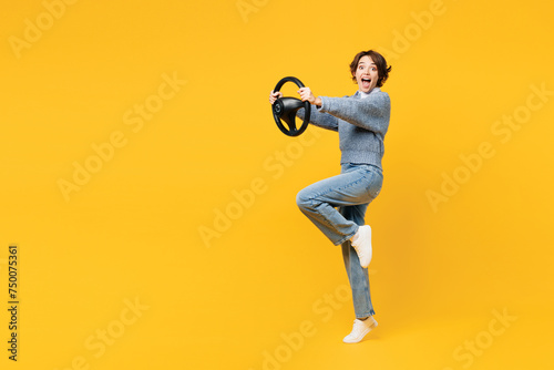 Full body side view surprised young woman she wearing grey knitted sweater shirt casual clothes hold steering wheel driving car isolated on plain yellow background studio portrait. Lifestyle concept.